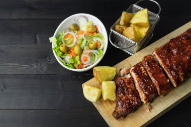 Barbekü pirzola, patates ve salata. Koyu bir arka planda tahta bir tahta üzerinde. Boşluğu kopyala.