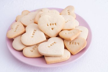 Kalp şeklinde kurabiyeli pembe tabak ve oymalı aşk kelimesi. Sevgililer Günü konsepti ve aşkı.