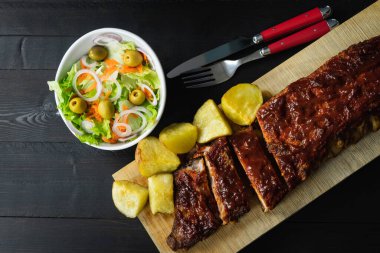 Barbekü soslu kaburgalar ve tahta tahtada siyah arka planda patatesler..