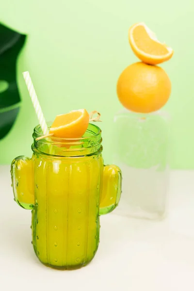 Cactus shaped glass with orange juice with fruit decoration on ice block. Copy space.