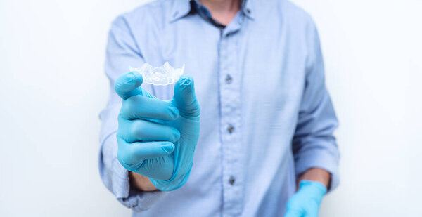 Dentist in gloves and blue shirt showing a clear dental splint. Copy space.