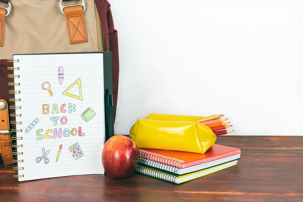 Notebook with back to school drawing. Backpack and school supplies with apple on white background. Copy space