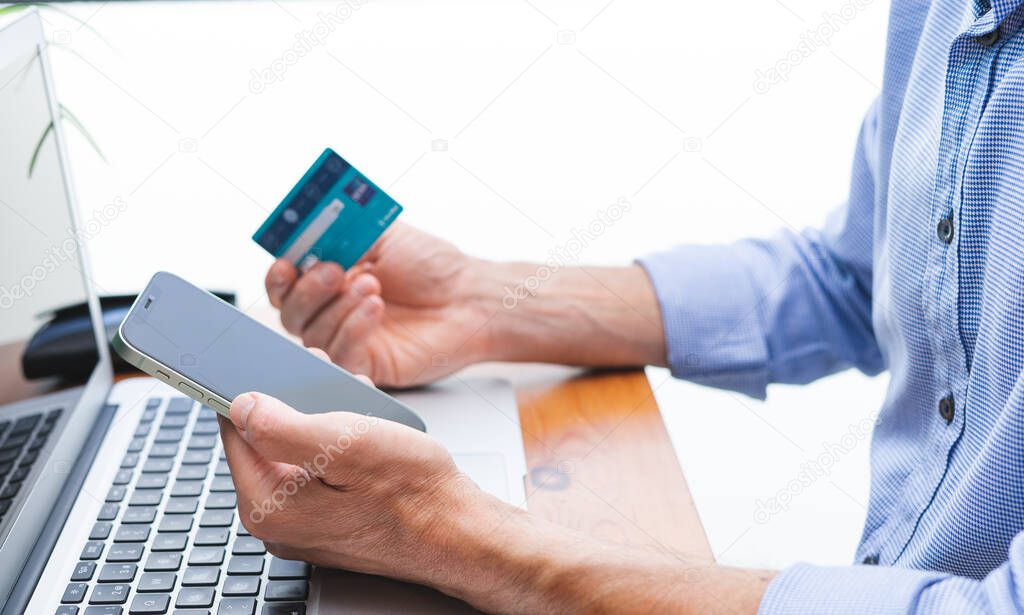 Man shopping and paying with cell phone and laptop and credit card. Copy space.