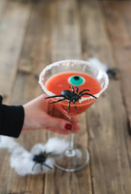 Kırsal ahşap arka planda Cadılar Bayramı için kırmızı renkli bir kokteyl tutan bir kadın. Uzayı kopyala Dikey fotoğraf.