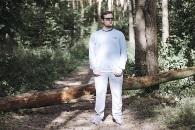 Gözlüklü bir adam devrilmiş bir ağaçta durup hayatı düşünür.