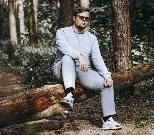 Gözlüklü bir adam devrilmiş bir ağaca oturur ve hayatı düşünür.