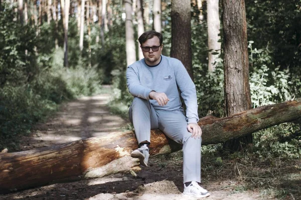 Gözlüklü bir adam devrilmiş bir ağaca oturur ve hayatı düşünür.