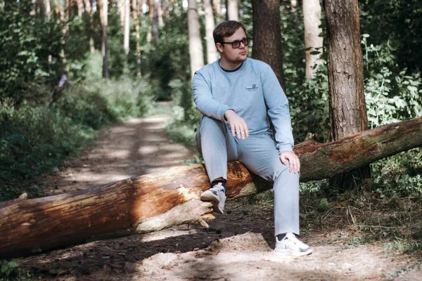 Gözlüklü bir adam devrilmiş bir ağaca oturur ve hayatı düşünür.