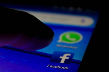 Alicante, İspanya - 6 Temmuz 2019: Mavi cep telefonu ekranında Facebook simgesine parmak basma. Arkaplanda Whatsapp simgesi.