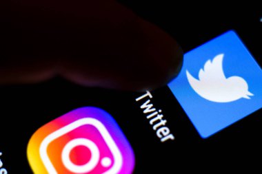Madrid, İspanya - 3 Mart 2021: Siyah cep telefonu ekranında Twitter simgesine parmak basma. Arkaplanda Instagram simgesi.