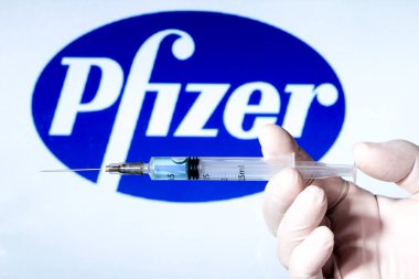 Madrid, İspanya... 7 Ocak 2020 'de elinde Covid aşısı olan beyaz ameliyat eldiveni vardı. Arka planda beyaz arkaplanda Pfizer Laboratuvarı logosu.