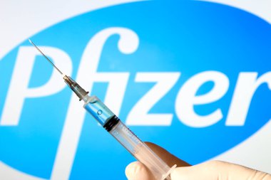 Madrid, İspanya... 7 Ocak 2020 'de elinde Covid aşısı olan beyaz ameliyat eldiveni vardı. Arka planda beyaz arkaplanda Pfizer Laboratuvarı logosu.