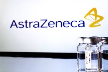 Madrid, İspanya 23 Şubat 2021 'de beyaz zemin üzerinde covid-19 aşısı olan cam şişeler. Arka planda Astrazeneca İlaç Şirketi logosu.
