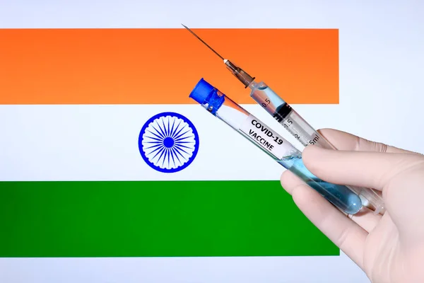 Hand in surgery glove holding syringe with covid vaccine. India\'s flag in the background