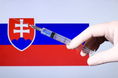 Ellerinde şırınga ve kovid aşısı olan eldiven var. Arka planda Slovakya bayrağı