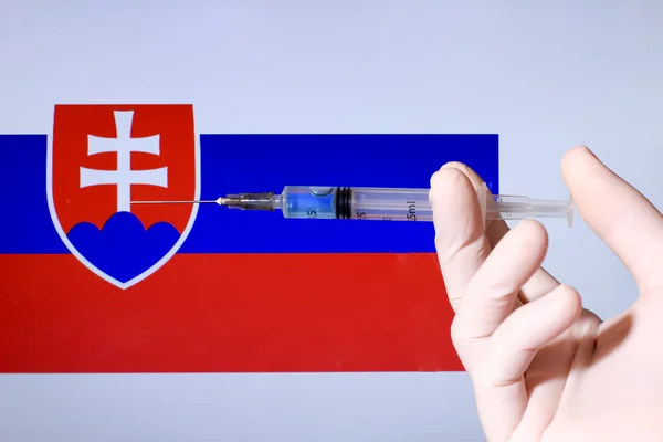Hand in surgery glove holding syringe with covid vaccine. Slovak flag in the background