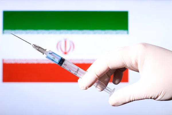 Hand in surgery glove holding syringe with covid vaccine. Iranian flag in the background