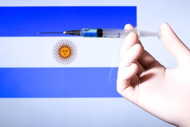 Ellerinde şırınga ve kovid aşısı olan eldiven var. Arjantin bayrağı arkada