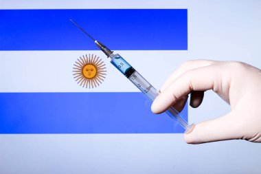 Ellerinde şırınga ve kovid aşısı olan eldiven var. Arjantin bayrağı arkada