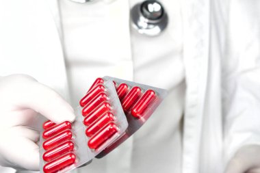 Beyaz ameliyat eldivenleri giymiş, steteskop takmış kırmızı kapsül kabarcıkları tutan bir doktor.