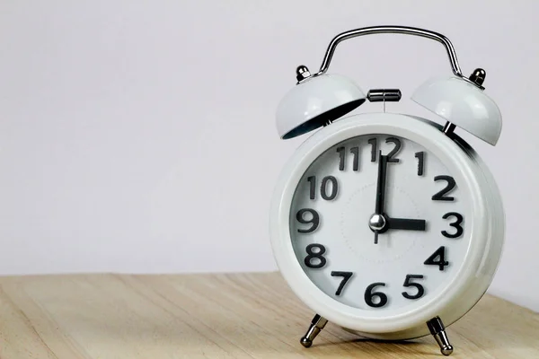 Old mechanical alarm clock on wooden table and white background showing three o\'clock