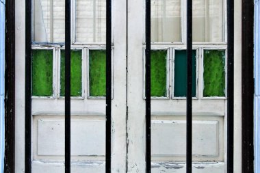 Yeşil boyalı camları ve sahte metal parmaklıkları olan beyaz ahşap bir pencere.