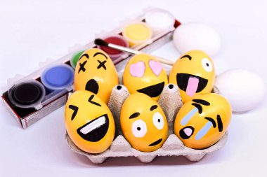 Alicante, Spain- March 18, 2021: Emoticons Easter Eggs in egg-cup , paints and brush with white background clipart