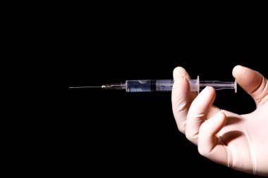 Siyah arka planda sıvı dolu bir şırıngayı tutan ellerin resmini kapat. 