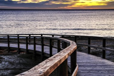 Arenales del Sol plajına giden ahşap patika. İspanya 'nın güneyinde Alicante' de gün doğumunun pembe ve turuncu renkleriyle güzel bir sahil.