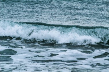 İspanya 'nın Alicante kentindeki La Marina plajında kışın bulutlu gökyüzünün altında dalgalı deniz.