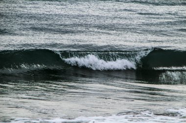 İspanya 'nın Alicante kentindeki La Marina plajında kışın bulutlu gökyüzünün altında dalgalı deniz.