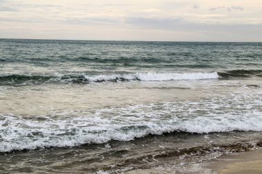 İspanya 'nın Alicante kentindeki La Marina plajında kışın bulutlu gökyüzünün altında dalgalı deniz.