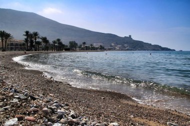 Güneşli bir günde İspanya, Murcia, Cartagena 'daki La Azohia köyünde tekneleri, uçurumları ve dağları olan güzel bir sahil.