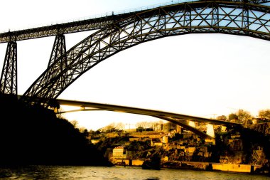 Gün batımında Porto 'daki Douro Nehri' nin suları üzerinde Maria Pia ve Ponte do Infante adında güzel ve devasa demir köprüler.