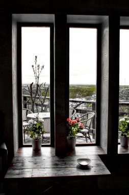 Gri gökyüzünün altındaki dağlar baharda pencereden görülür. Tahta masa ve saksılar ön planda.