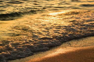 Gün batımında kumsalda renkli dalgalar ve kum dokusu