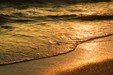 Gün batımında kumsalda renkli dalgalar ve kum dokusu