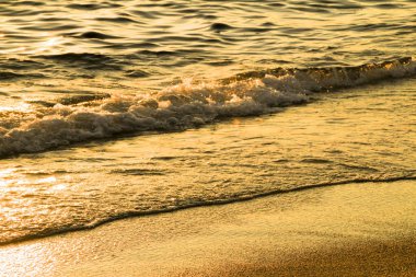 Gün batımında kumsalda renkli dalgalar ve kum dokusu