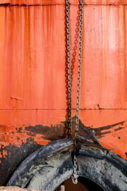 Denia, Alicante, İspanya 'daki eski teknenin paslı turuncu yüzeyinde eski lastikleri tutan zincirler.