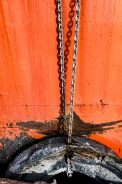 Denia, Alicante, İspanya 'daki eski teknenin paslı turuncu yüzeyinde eski lastikleri tutan zincirler.