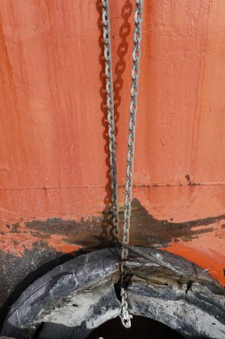 Denia, Alicante, İspanya 'daki eski teknenin paslı turuncu yüzeyinde eski lastikleri tutan zincirler.
