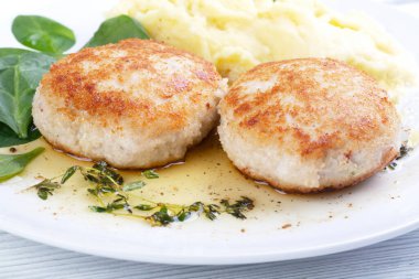 Tavuk pirzolası, patates püresi ve beyaz tabakta ıspanak.