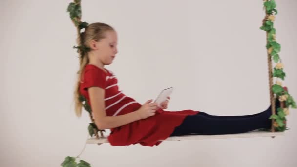 Child sitting on swing with digital tablet — Stock Video