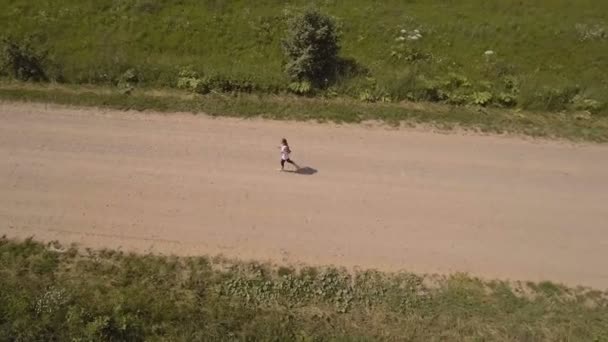 Meisje draait op de weg in een veld. Luchtfoto. — Stockvideo