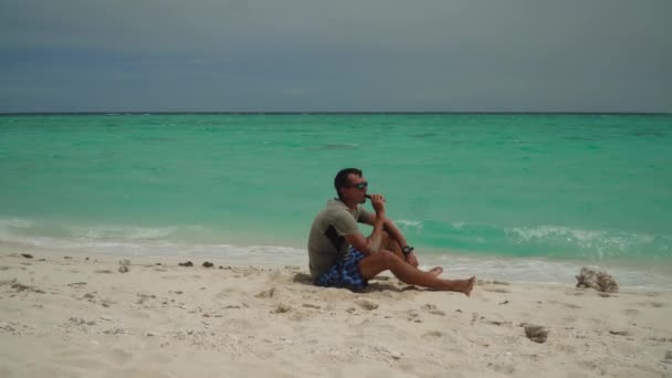 A man sits on a tropical beach. — Stock Video