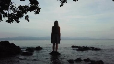 Bir kadın kumsalda gün batımından hoşlanır..