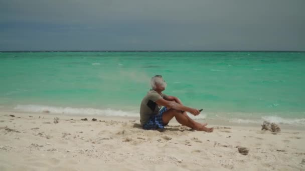 A man sits on a tropical beach. — Stock Video