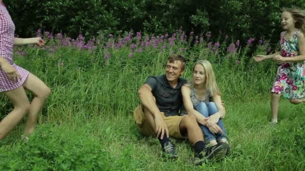 Glückliche vierköpfige Familie sitzt an einem Sommertag im Gras — Stockvideo