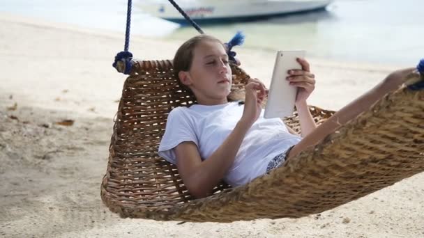 Дівчина в гамаку з планшетом на пляжі — стокове відео