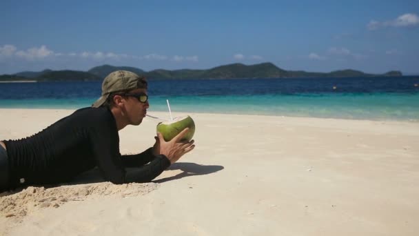 Hombre en la playa bebiendo jugo de coco — Vídeo de stock